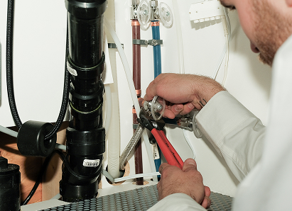 Using two pipe wrenches, a Anchor Home Comfort professional plumber services a pipe connection near a vertical flue or vent pipe.